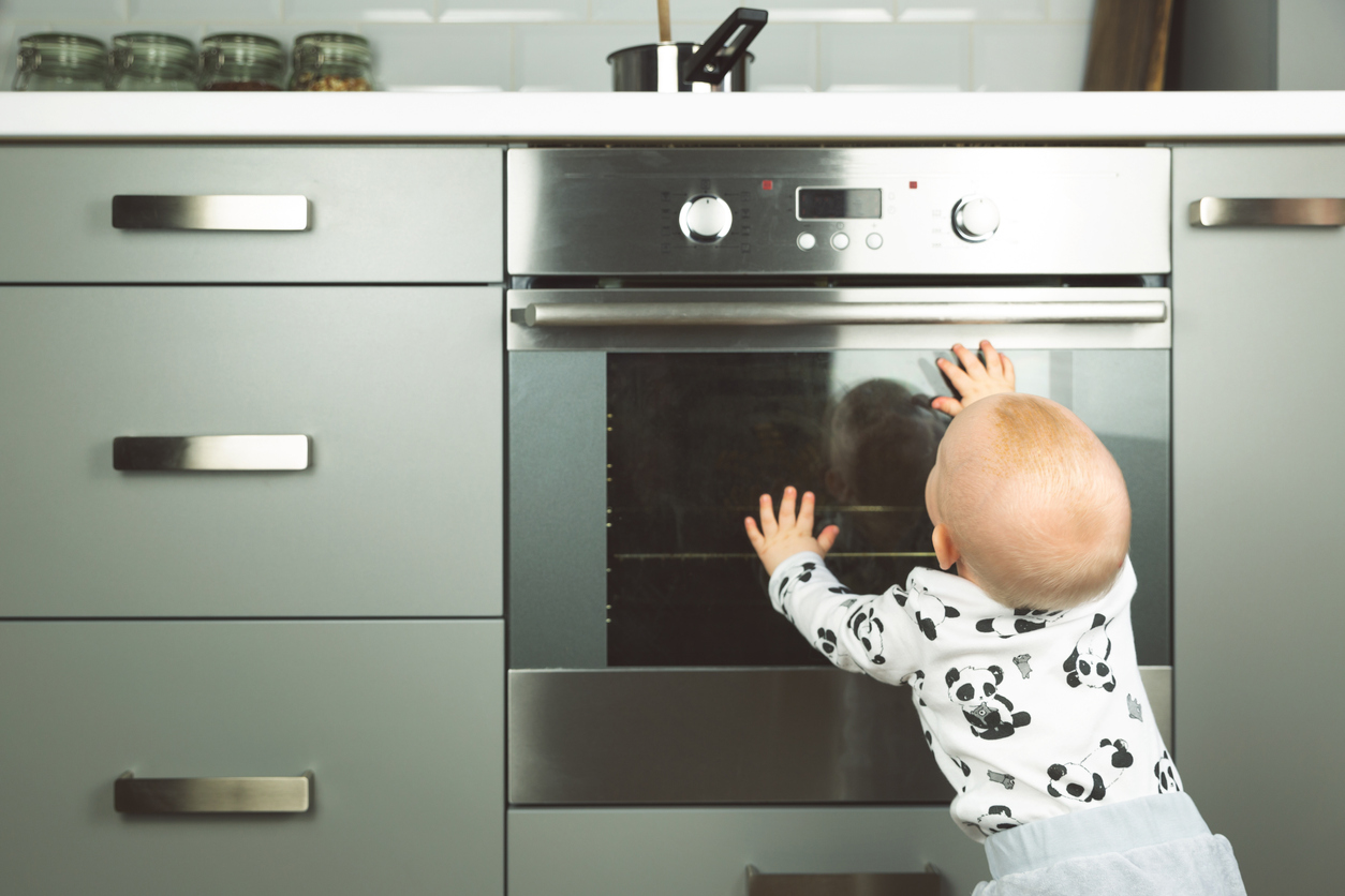 Little child playing with electric stove in the kitchen. Baby safety in kitchen